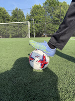 Player resting foot on Strykr Flight Pro Premier League style soccer ball on turf